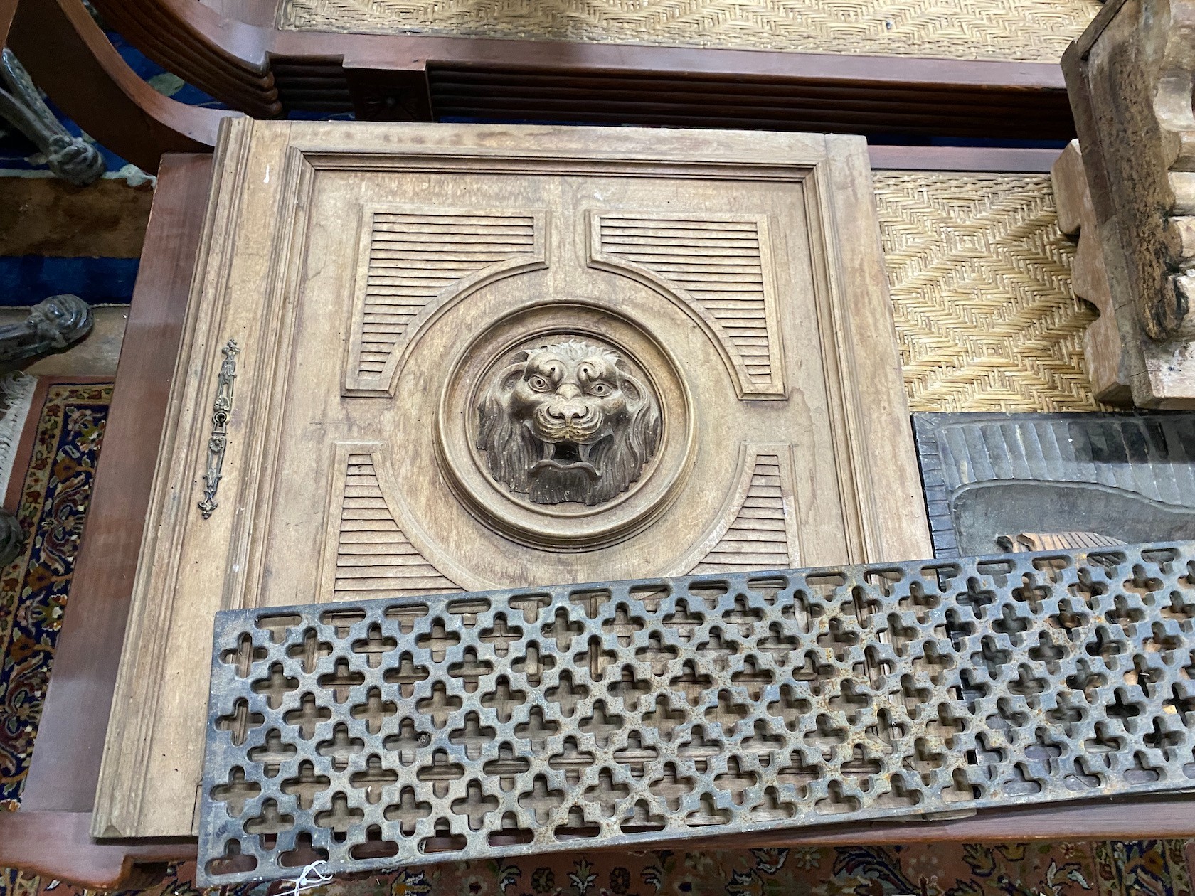 An Asian hardwood low seat, a relief carved panel, a lion's mask carved door and a cast iron grate